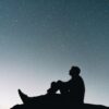 a man sitting on top of a hill under a night sky