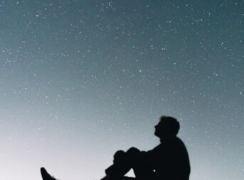 a man sitting on top of a hill under a night sky